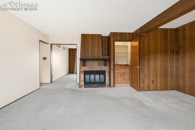 unfurnished living room featuring a tiled fireplace, wooden walls, and light colored carpet