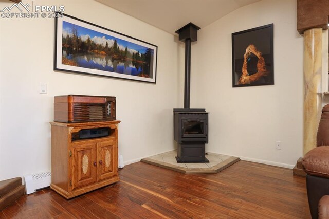 living room featuring dark wood-type flooring, a baseboard radiator, vaulted ceiling, and a wood stove