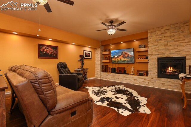 cinema room featuring a stone fireplace, wood-type flooring, and ceiling fan