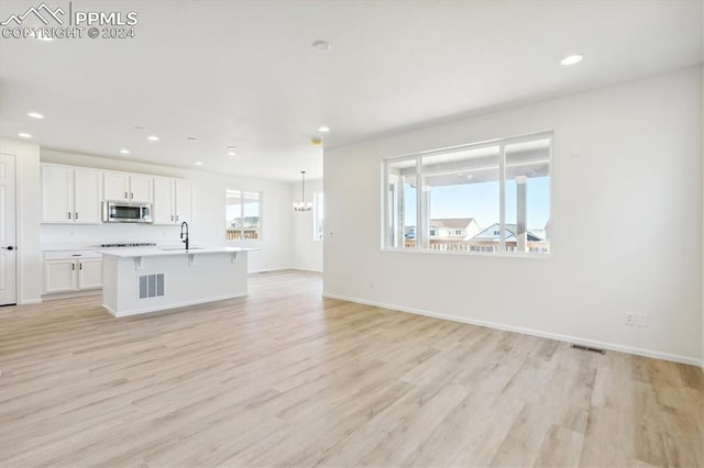 unfurnished living room with light wood-type flooring, sink, and an inviting chandelier