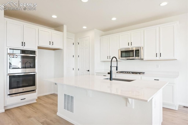 kitchen featuring white cabinetry, sink, a center island with sink, appliances with stainless steel finishes, and light wood-type flooring