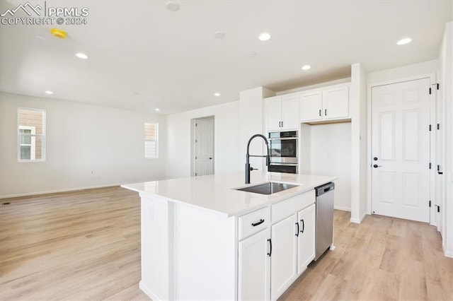 kitchen featuring stainless steel dishwasher, sink, light hardwood / wood-style flooring, white cabinets, and an island with sink