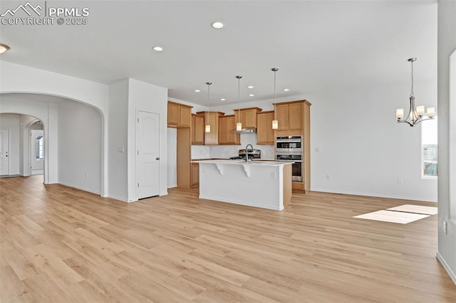 kitchen with open floor plan, arched walkways, light countertops, light wood-type flooring, and recessed lighting