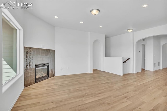 unfurnished living room featuring recessed lighting, light wood-type flooring, arched walkways, a tile fireplace, and baseboards