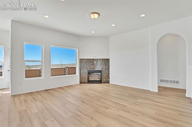 unfurnished living room featuring light wood finished floors, arched walkways, a tile fireplace, recessed lighting, and baseboards
