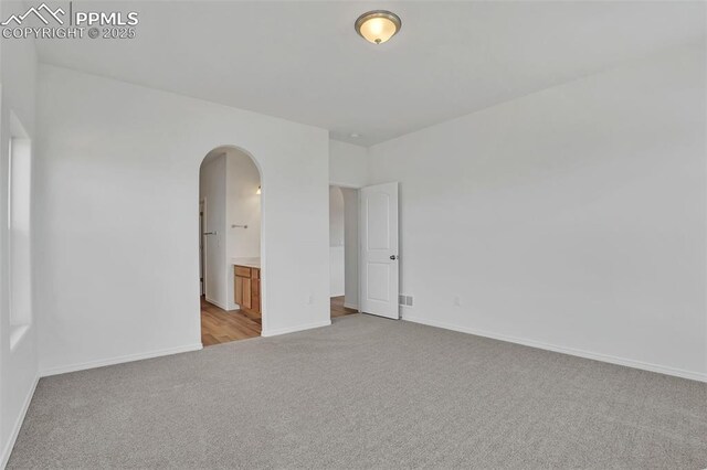 unfurnished room with light carpet, arched walkways, and baseboards