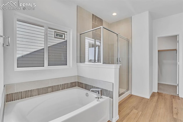 bathroom featuring a stall shower, a walk in closet, a garden tub, wood finished floors, and baseboards