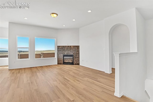 unfurnished living room featuring light wood-type flooring, a tile fireplace, recessed lighting, and baseboards