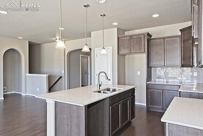 kitchen with sink, pendant lighting, decorative backsplash, dark hardwood / wood-style floors, and an island with sink