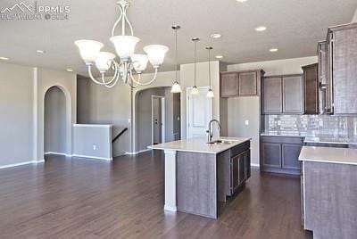 kitchen with dark wood-type flooring, sink, backsplash, and a kitchen island with sink