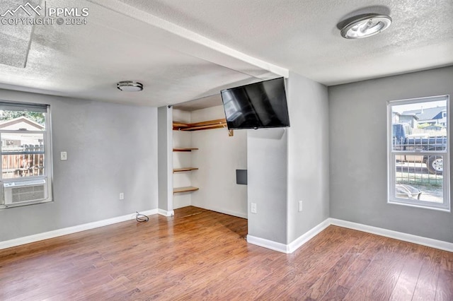 interior space with a textured ceiling, cooling unit, and wood-type flooring