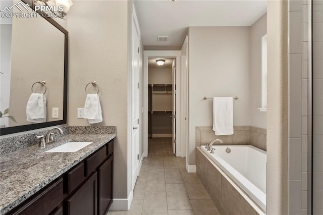 bathroom featuring a relaxing tiled tub, tile patterned flooring, and vanity