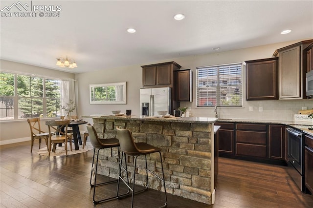 kitchen with dark brown cabinets, dark wood-type flooring, light stone countertops, and stainless steel appliances