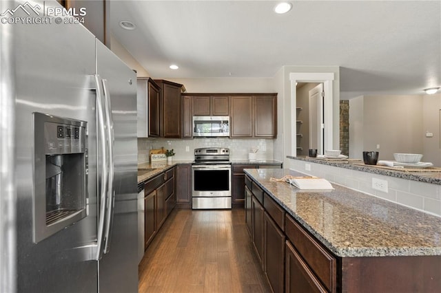 kitchen with light stone countertops, backsplash, stainless steel appliances, and wood-type flooring