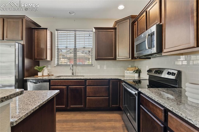 kitchen featuring decorative backsplash, wood-type flooring, appliances with stainless steel finishes, light stone counters, and sink