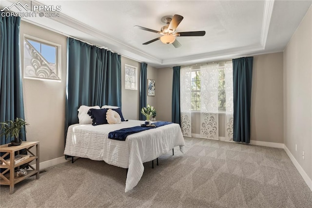 carpeted bedroom with ceiling fan, a tray ceiling, ornamental molding, and multiple windows