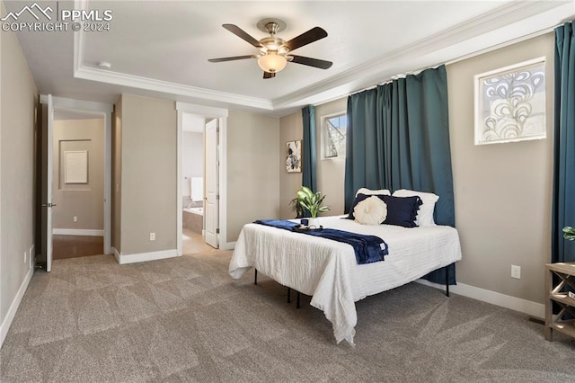 carpeted bedroom with ceiling fan, a raised ceiling, crown molding, and ensuite bath