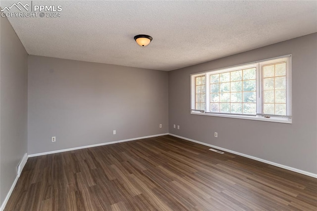 spare room with a textured ceiling and dark hardwood / wood-style flooring