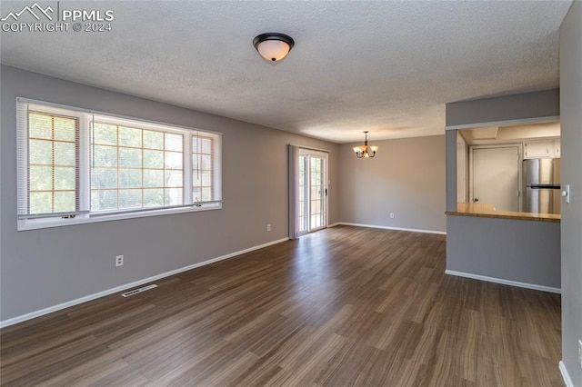 unfurnished room featuring a textured ceiling, a notable chandelier, and dark hardwood / wood-style floors