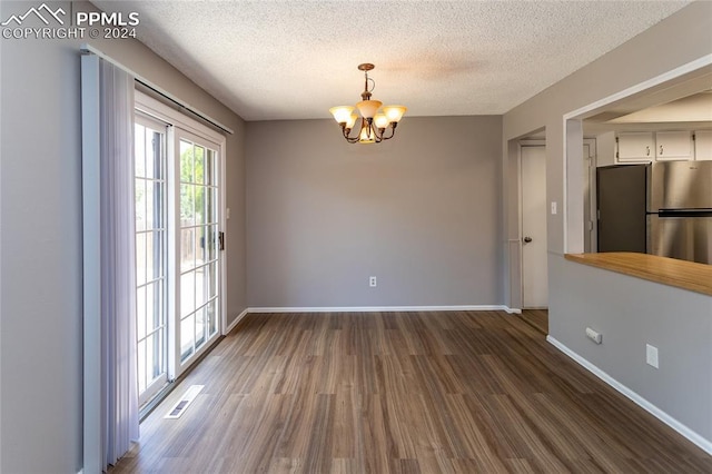 unfurnished dining area featuring a textured ceiling, dark wood-type flooring, and an inviting chandelier