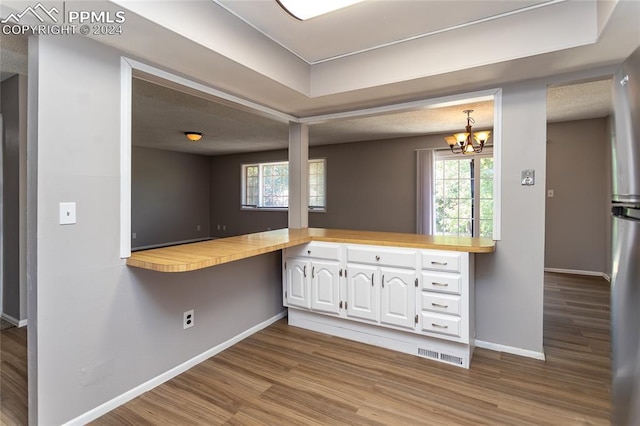 kitchen featuring wooden counters, light wood-type flooring, kitchen peninsula, white cabinets, and an inviting chandelier