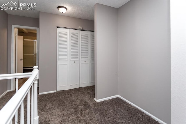 unfurnished bedroom featuring dark carpet, a closet, and a textured ceiling