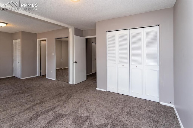 unfurnished bedroom with a textured ceiling, multiple closets, and dark colored carpet