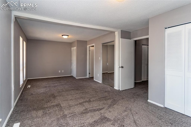 unfurnished bedroom with a textured ceiling, two closets, and dark carpet