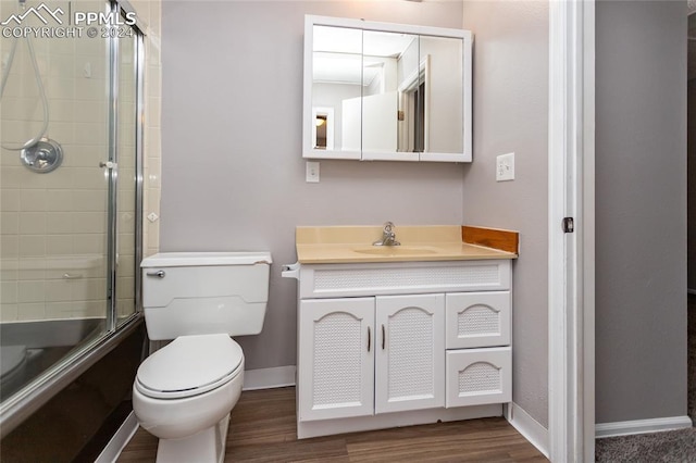 full bathroom featuring toilet, enclosed tub / shower combo, wood-type flooring, and vanity