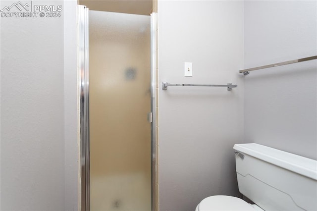 bathroom featuring a shower with door and toilet