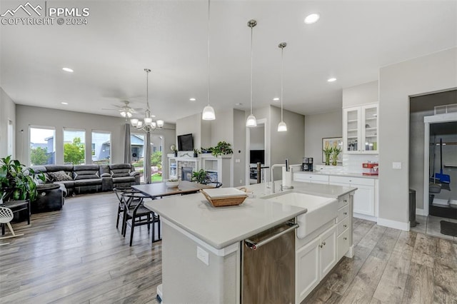 kitchen featuring white cabinets, a kitchen island with sink, stainless steel dishwasher, light hardwood / wood-style floors, and pendant lighting