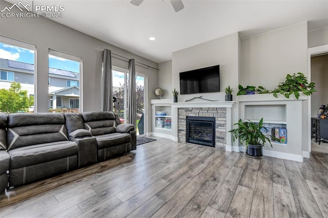 living room featuring ceiling fan, hardwood / wood-style flooring, and a stone fireplace