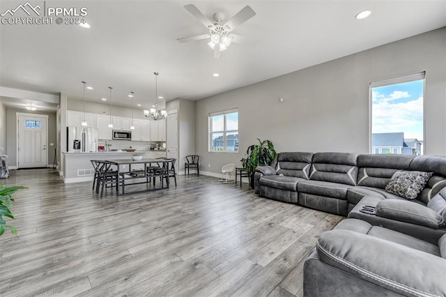 living room with ceiling fan with notable chandelier and light hardwood / wood-style flooring