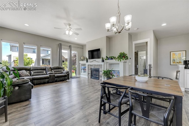 dining room with a wealth of natural light, a fireplace, ceiling fan with notable chandelier, and hardwood / wood-style floors