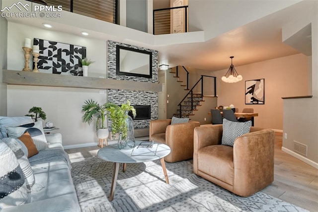 living room featuring a notable chandelier, a high ceiling, a tile fireplace, and light wood-type flooring