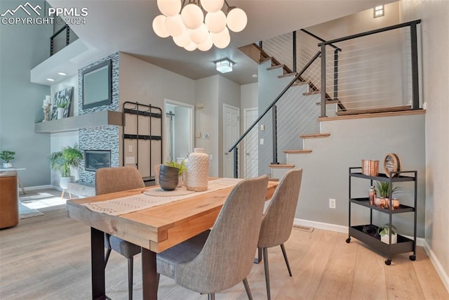 dining space featuring a tiled fireplace, light hardwood / wood-style flooring, and an inviting chandelier