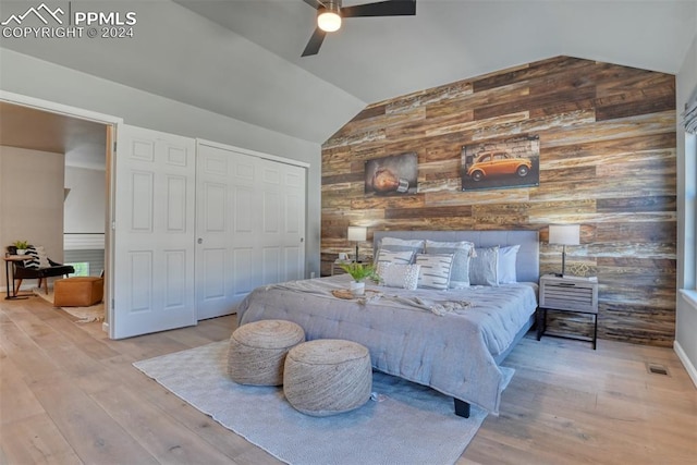 bedroom featuring vaulted ceiling, light wood-type flooring, wooden walls, and a closet