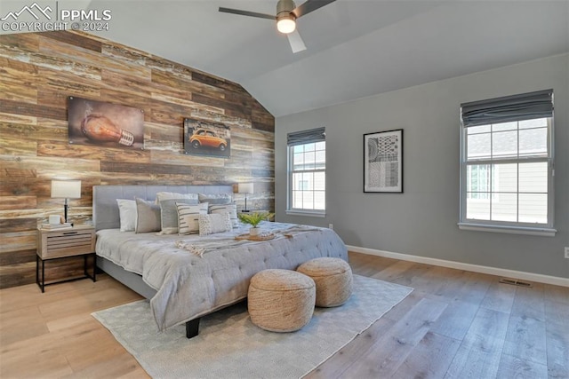 bedroom featuring light hardwood / wood-style flooring, wood walls, ceiling fan, and vaulted ceiling