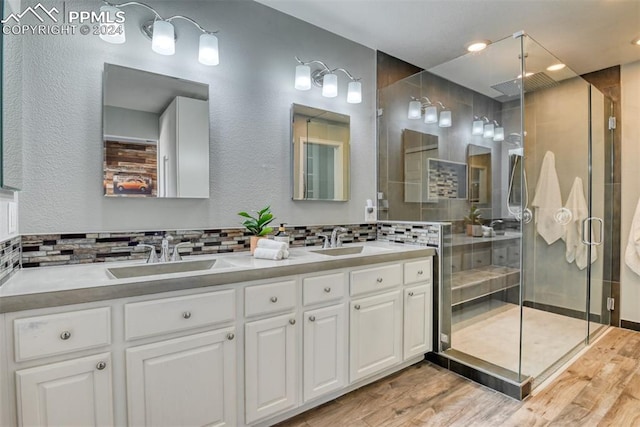 bathroom featuring wood-type flooring, an enclosed shower, vanity, and backsplash