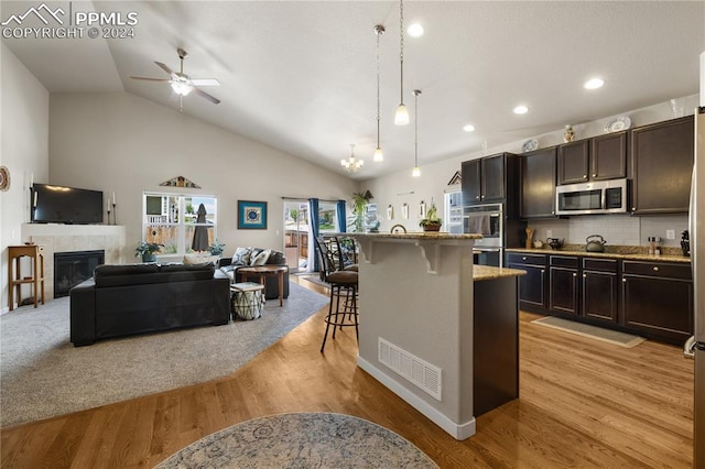 kitchen featuring a breakfast bar area, light wood-type flooring, ceiling fan with notable chandelier, stainless steel appliances, and a tiled fireplace