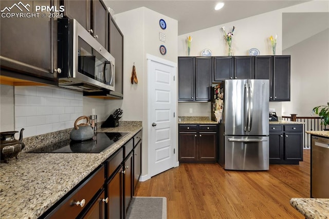 kitchen featuring stainless steel appliances, light stone counters, light hardwood / wood-style floors, decorative backsplash, and lofted ceiling