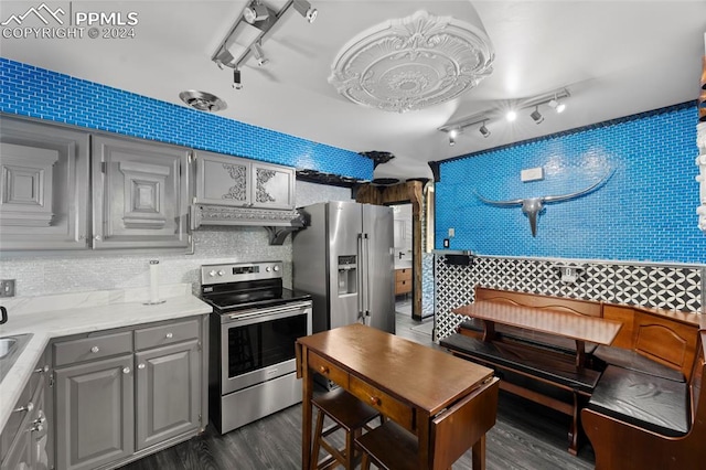 kitchen with appliances with stainless steel finishes, gray cabinets, rail lighting, ventilation hood, and dark wood-type flooring