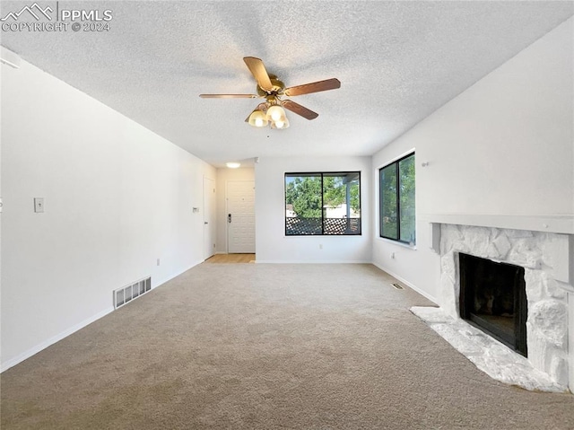 unfurnished living room featuring ceiling fan, a stone fireplace, light carpet, and a textured ceiling