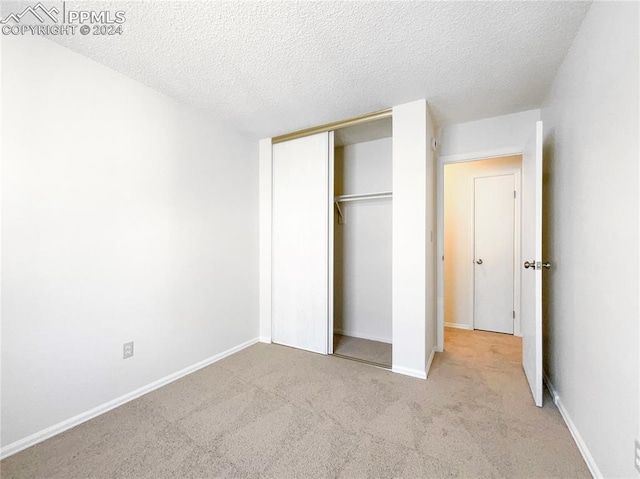 unfurnished bedroom with a closet, light carpet, and a textured ceiling