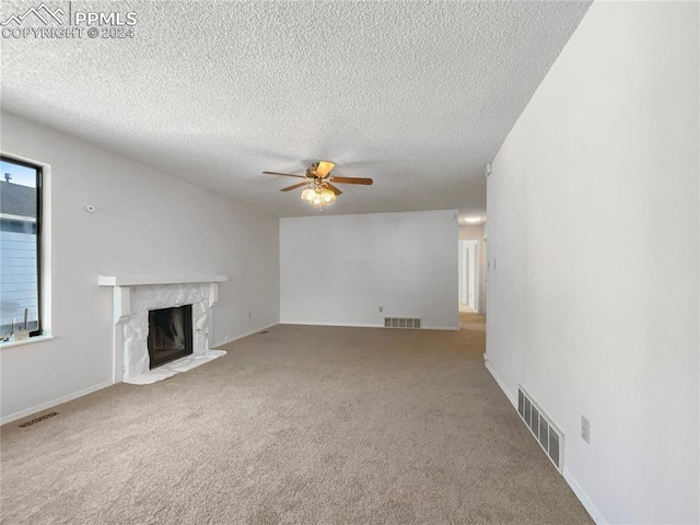 unfurnished living room with a premium fireplace, carpet floors, ceiling fan, and a textured ceiling