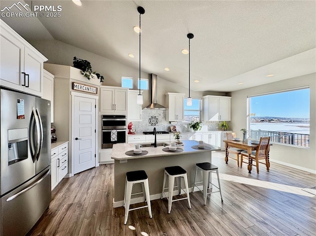 kitchen with appliances with stainless steel finishes, white cabinetry, a kitchen island with sink, a water view, and wall chimney exhaust hood