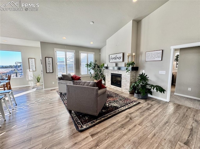 living room with a stone fireplace, a textured ceiling, lofted ceiling, and light hardwood / wood-style floors