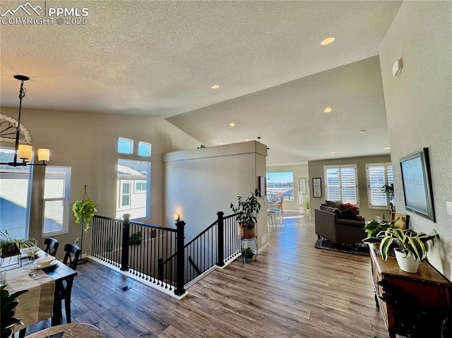 corridor with a notable chandelier, hardwood / wood-style flooring, vaulted ceiling, and a textured ceiling