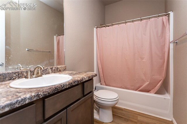 full bathroom featuring toilet, shower / bath combination with curtain, hardwood / wood-style flooring, and vanity