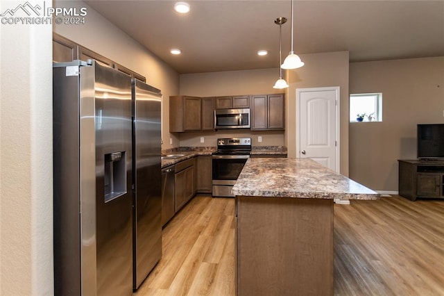 kitchen with a kitchen island, stainless steel appliances, decorative light fixtures, and light wood-type flooring